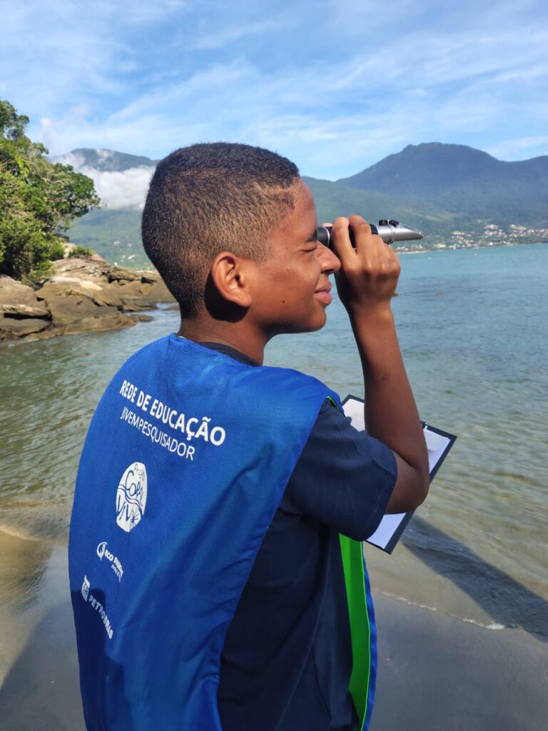 Estudante participante do programa Jovens Naturalistas realizando análise com refratômetro na praia