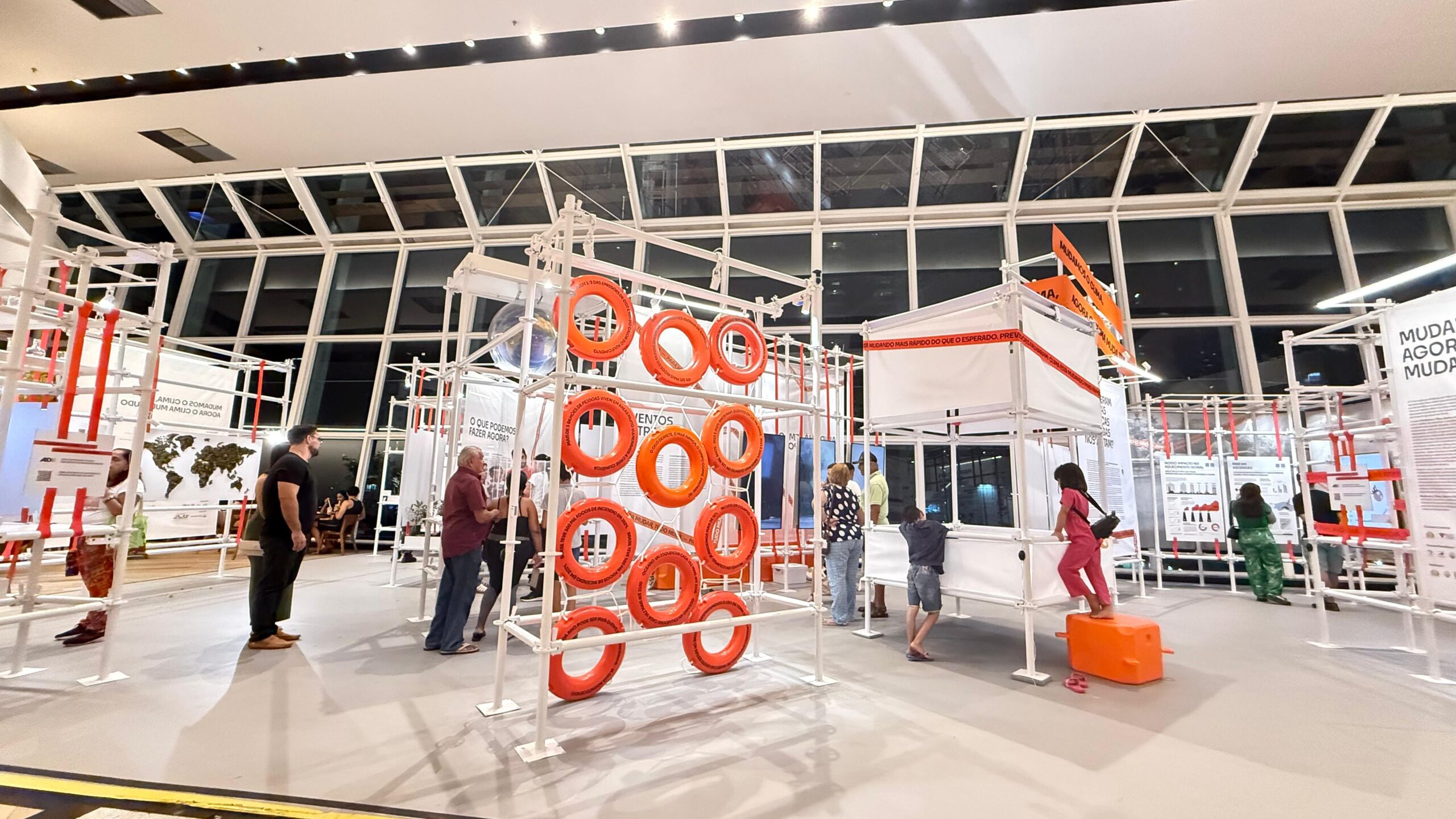 Estrutura da exposição em corredor de shopping com painéis ilustrados sobre corais, teto decorado com esculturas suspensas e piso com adesivação azul lembrando o fundo do mar.