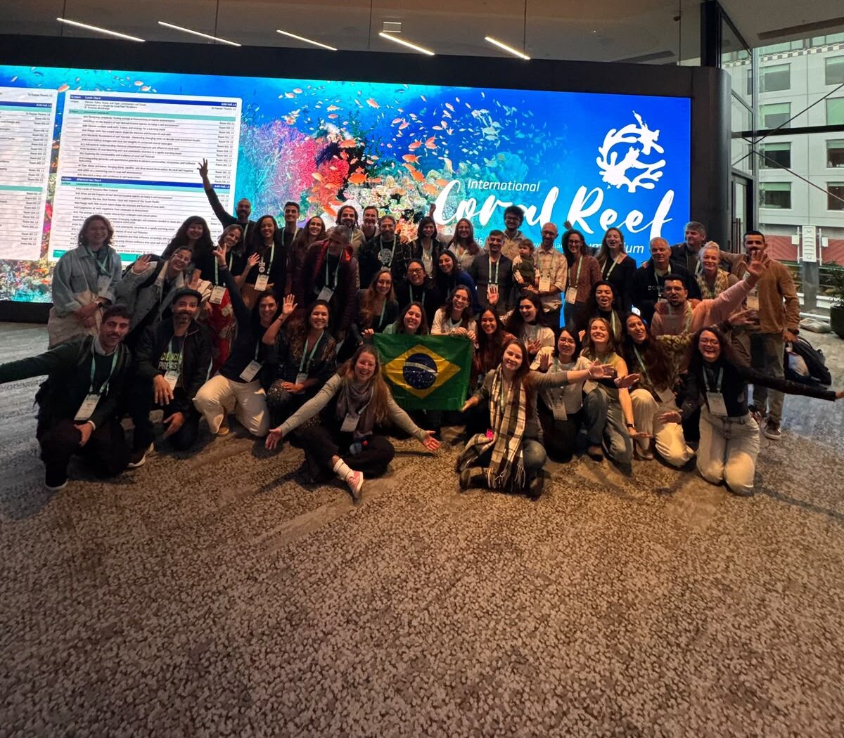 Fotografia da delegação do Projeto Coral Vivo reunida no evento ICRS 2026 segurando a bandeira do Brasil.