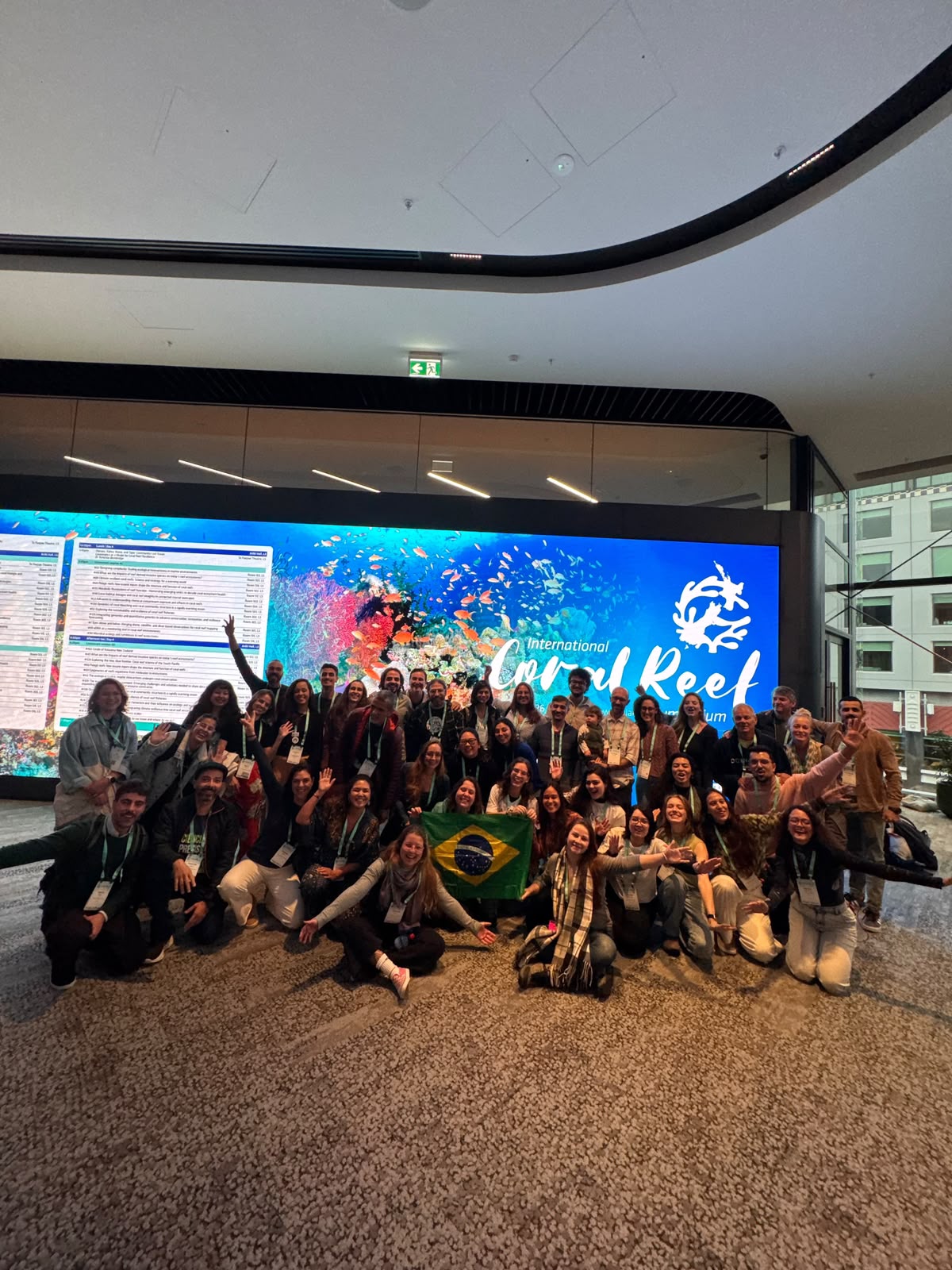 Fotografia da delegação do Projeto Coral Vivo reunida no evento ICRS 2026 segurando a bandeira do Brasil.