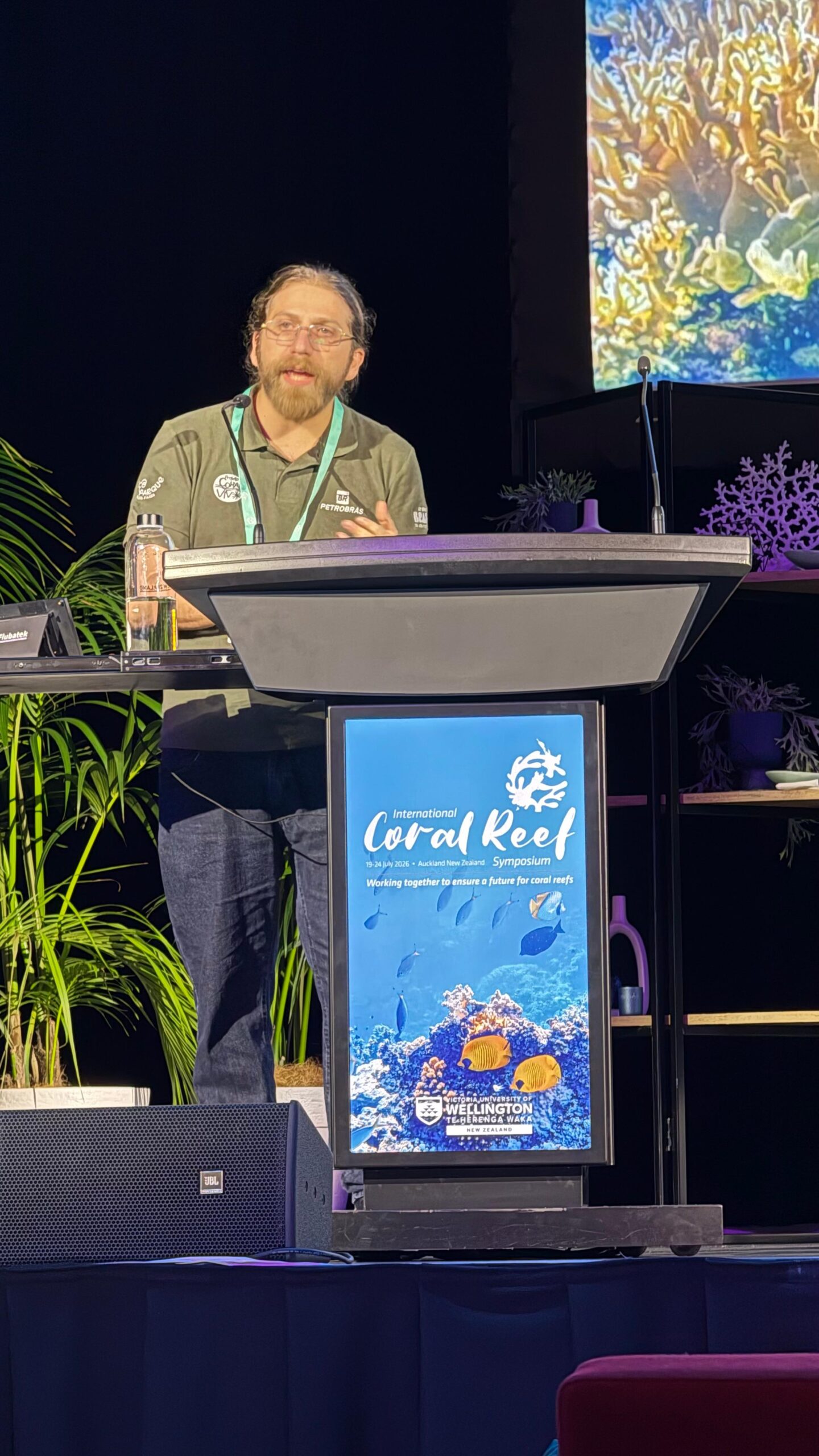 Pesquisador Miguel Mies discursando no pódio pelo Projeto Coral Vivo no ICRS 2026.
